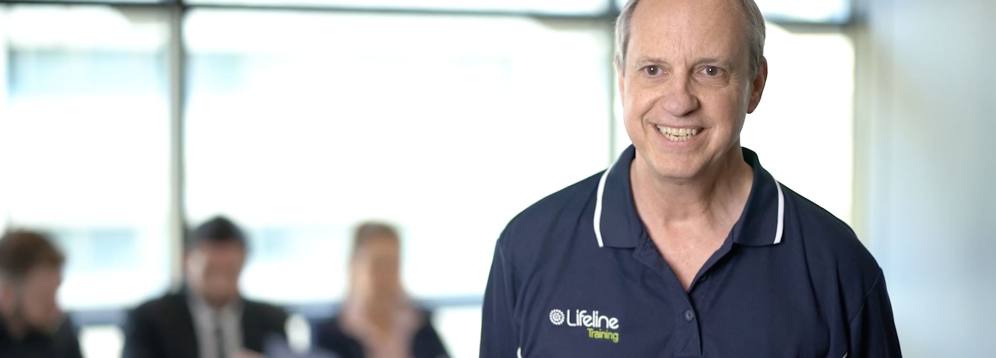 A Lifeline Training educator smiles as workplace training participants sit in the background.